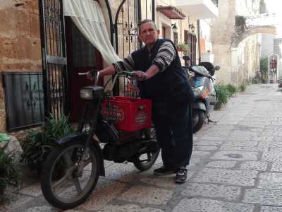 � un uomo di bassa statura e grossa corporatura ed � vestito con scarpe anti infortunio scure, jeans, maglione a righe, gilet con tasche e un borsello di pelle scura, l� dove ripone i suoi guadagni